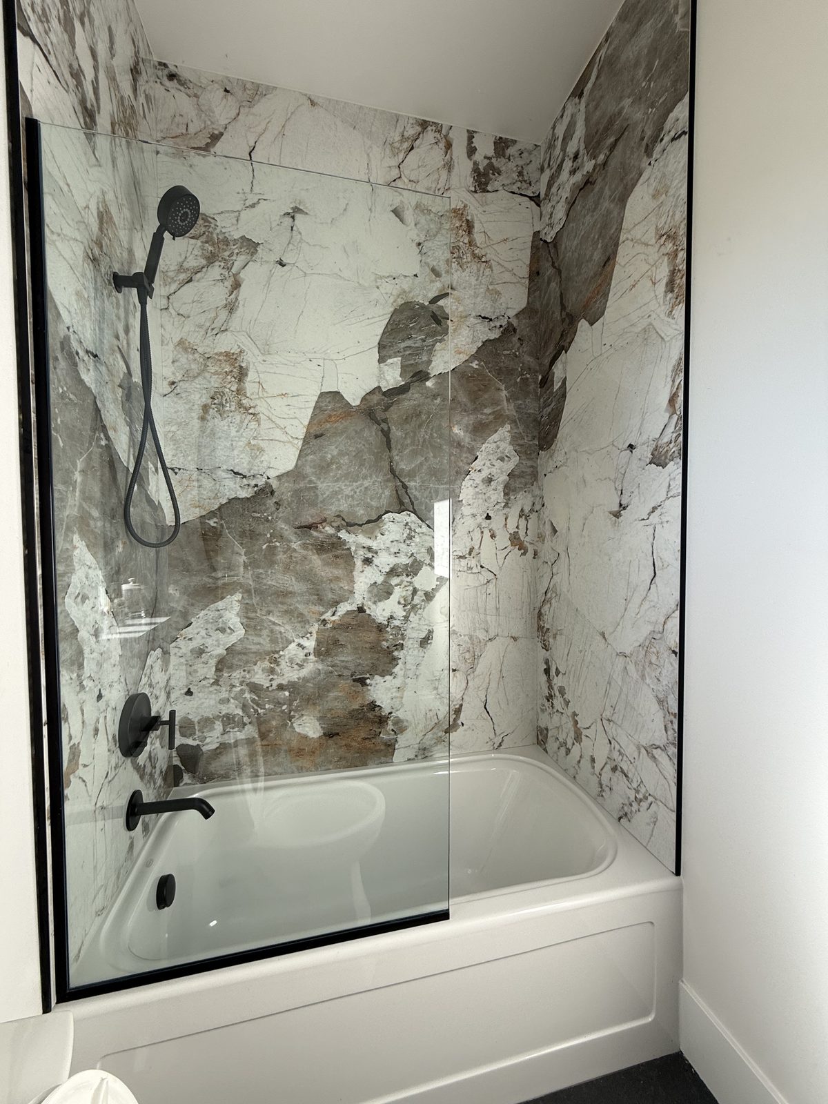 Patagonia porcelain slab walls around a tub, with matte black hardware and a black-framed glass panel