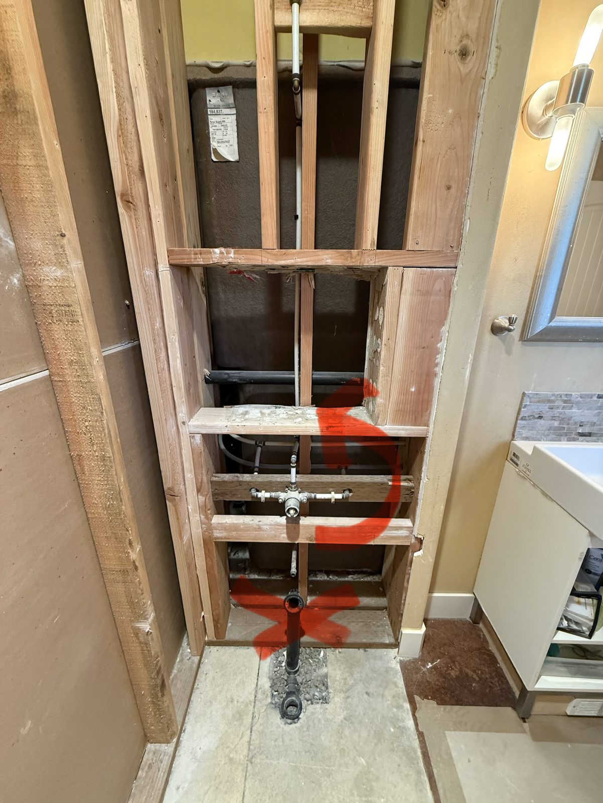 Open wall showing the shower valve at tub height, marked to be raised, with the old tub plumbing marked for removal