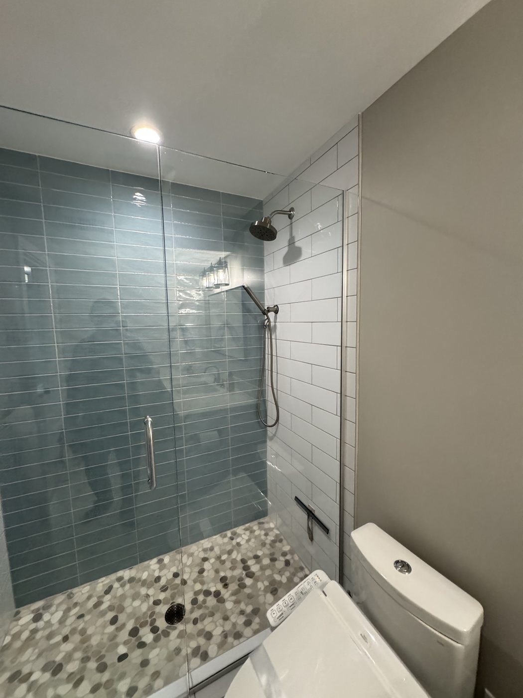 Shower with vertical blue tile, white subway tile, and a pebble floor