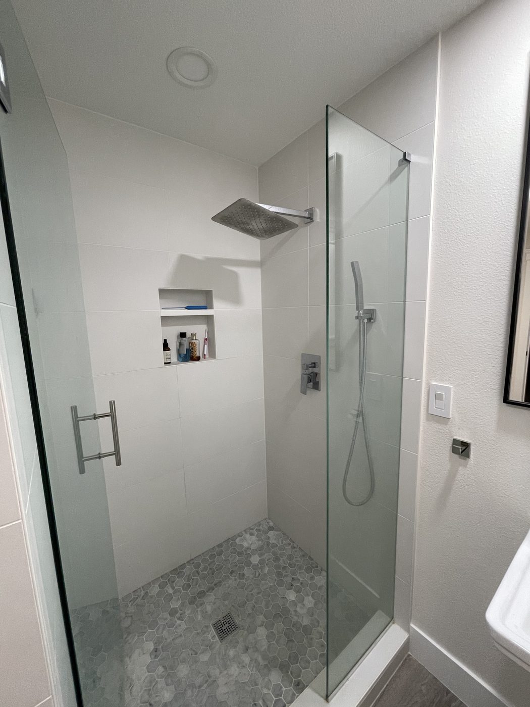 White tiled shower with a hexagon mosaic floor and recessed niche
