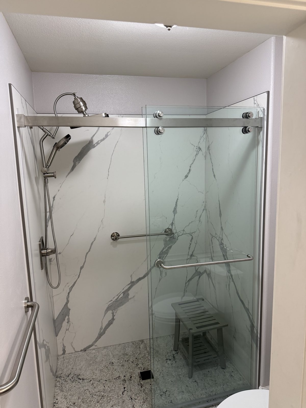 Finished walk-in shower with marble-look stone walls, grab bars, a seat, and sliding frameless glass