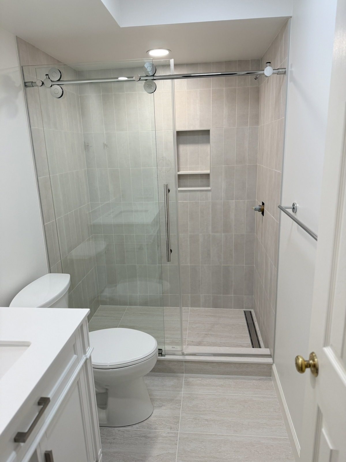 Tiled walk-in shower with recessed niche, linear drain, and chrome sliding frameless glass